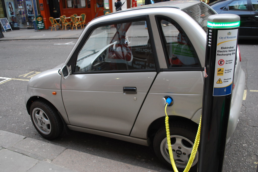 An electric car charging beside a petrol pump