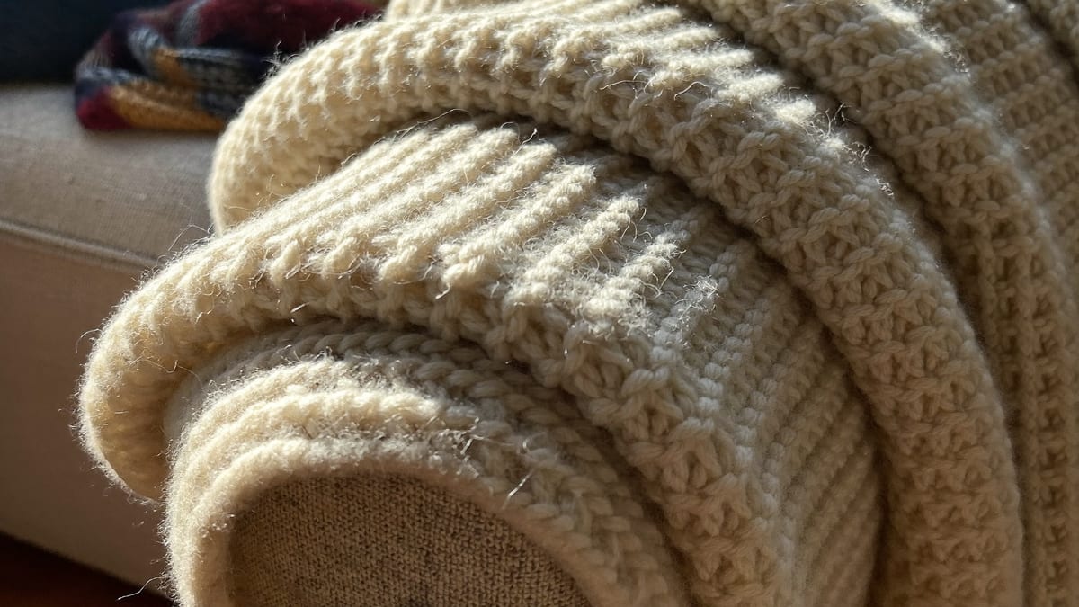 A knitted wool blanket folded over the arm of a sofa