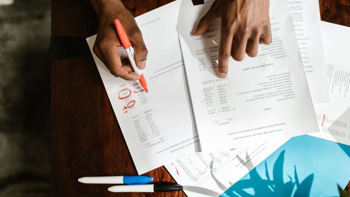 Hands marking up printed statements with a red pen