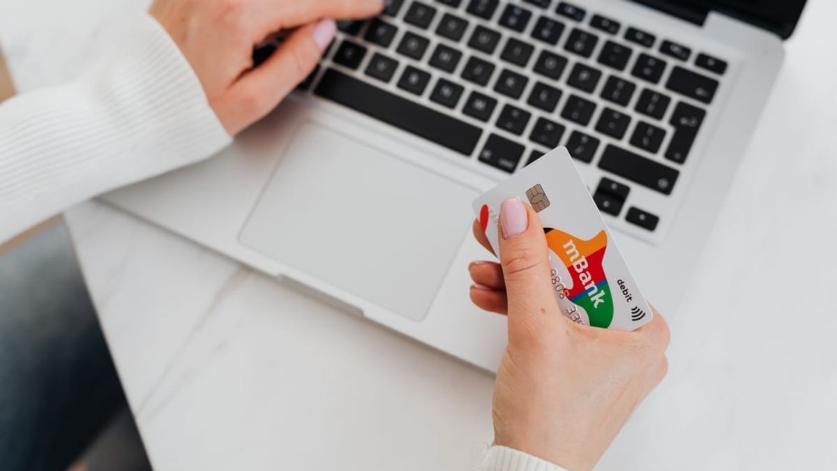 A hand holding a payment card beside a laptop