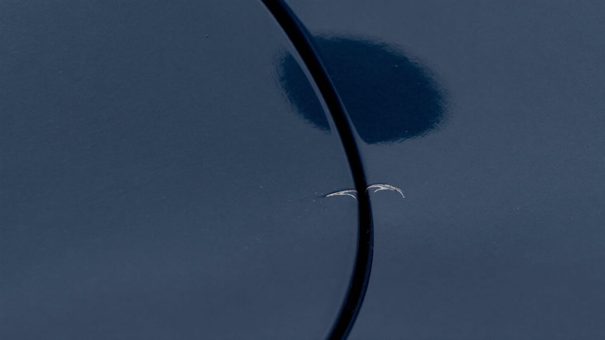 A small scratch in dark car paint beside a panel gap